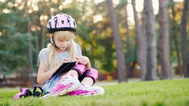 The girl is sitting near the house, enjoying the tablet. Rolled on roller skates - on her helmet and rollers