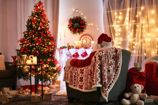 Authentic Santa Claus sitting in armchair at room decorated for Christmas