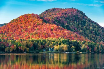 Crédence de cuisine en verre imprimé Canada Les collines couvertes de forêts d& 39 érables rouges derrière une maison en bois au bord d& 39 un lac au Québec, par une belle soirée d& 39 automne.