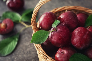 Wicker basket with fresh ripe plums on table, closeup