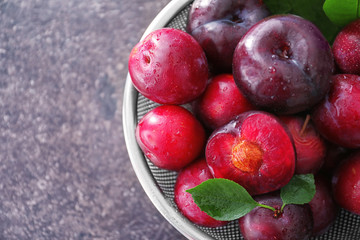 Sieve with fresh ripe plums on table, closeup