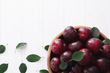 Bowl with fresh ripe plums on white background