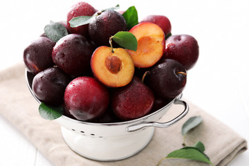Collander with fresh ripe plums on white background