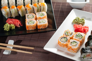 Sushi rolls on a black and white plate, on a wooden mat with chopsticks and soy sauce