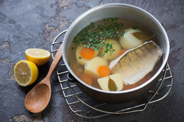 Metal pot with freshly made fish soup or russian ukha on a stone background, studio shot