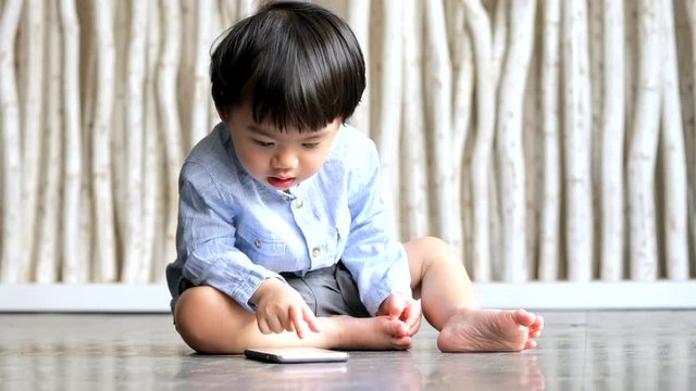 Little boy watching on cellphone and sitting on the floor