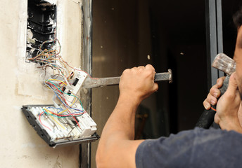 Bricklayer opening a hole with hammer and chisel in the wall