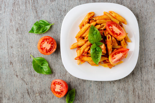 Penne with tomato sauce and basil on wooden background, top view.