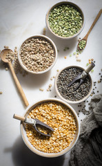 Brown lentil,French lentil Split dry green peas and Split chana dal in individual ceramic bowls on a marble backdrop on top down ingredient shot
