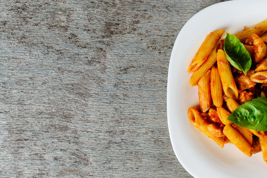 Penne with tomato sauce and basil on wooden background, top view