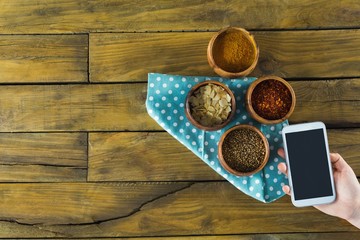 Hand holding mobilephone and various spices in bowl