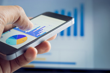 Businessman hand holding smartphone with graph chart on laptop background.For business market  concept