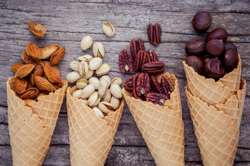 Concept for homemade various nuts ice cream. Mixed nuts in waffle cones on shabby wooden background.top view