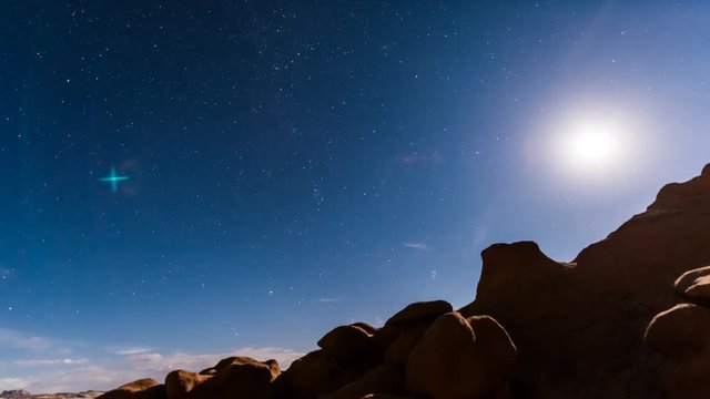 Timelapse footage of night sky with full moon rising, or moonrise, in Goblin Valley State Park in Utah showing clouds, stars, and canyons silhouettes in wilderness nature