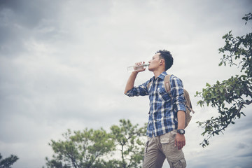 Happy hipster man tourist with backpack drinking water while hiking in nature forest.