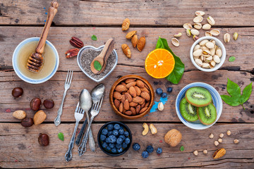 Ingredients for a healthy foods background, nuts, honey, berries, fruits, blueberry, orange, almonds, walnuts and chia seeds .The concept of healthy food set up on shabby wooden background. Flat lay.