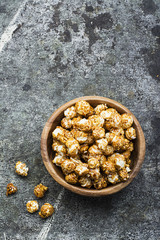 A wooden bowl with caramelized popcorn on a gray grunge trend background. Top View.