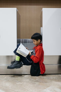 A young boy working on word puzzles at an empty check-in counter at the airport