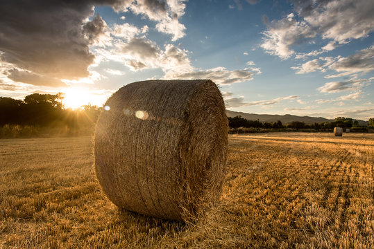 Straw bales below a cloudy sky at sunset