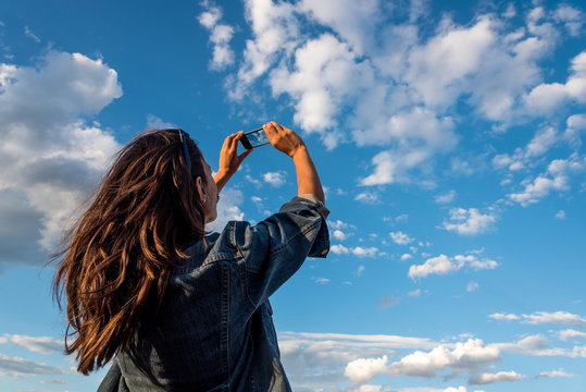 Beauty young woman taking pictures of a cloudy sky with a smartphone