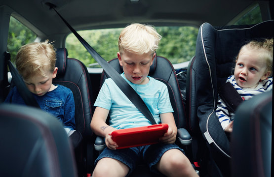 Children using electronic tablets while sat in the car