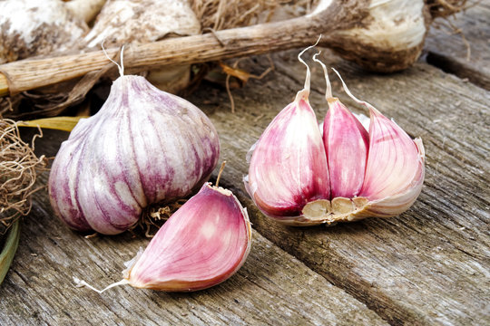 Whole garlic with broken bulb and pink cloves on rustic wooden board.