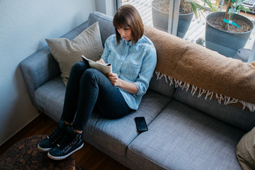 Young female entrepreneur works on business homework study fro home on couch with mobile phone