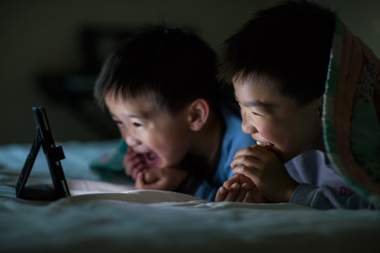 Asian kids watching on tablet computer in bed at home