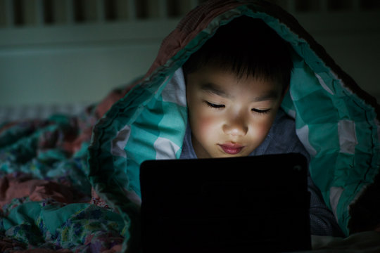 Asian kid playing with tablet computer in bed at home