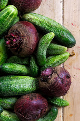 Freshly harvested pickling cucumbers and beetroots on light wooden board from above.