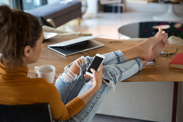 Beautiful young smiling woman looking at her smart phone while sitting comfortably