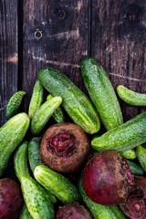 Freshly harvested pickling cucumbers and beetroots on dark rustic wooden board from above. Space for text.