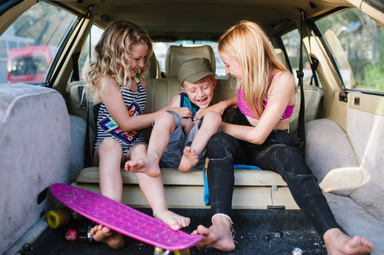 Sisters tickling their little brother in back of car