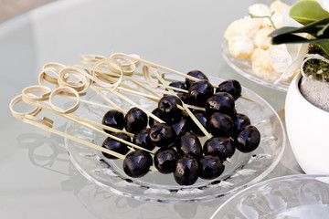 Black olives on bamboo party sticks lying on glass plate.