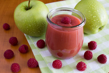 Puree with apples and raspberries  in the glass  jar on the table
