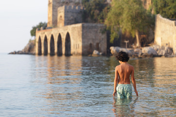 Fototapeta na wymiar Backview portrait of a boy in swimwear near Alanya medieval ship
