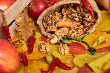 Nuts in a sack, fruits and vegetables on fallen leaves background, autumn season