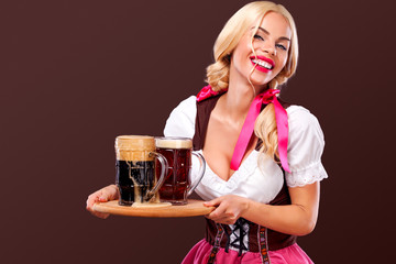 Closeup portrait of Oktober fest girl - waitress, wearing a traditional Bavarian dress, serving big beer mugs on brown background.