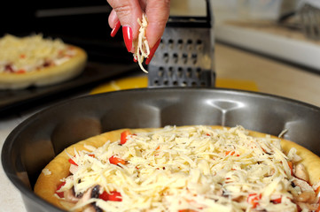A female hand sprinkles a pizza with grated cheese close-up.