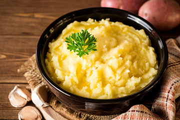 Mashed potatoes with butter and fresh parsley in bowl on rustic wooden table