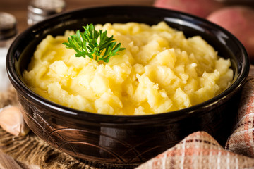 Mashed potatoes with butter and fresh parsley in bowl on rustic wooden table