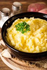 Mashed potatoes with butter and fresh parsley in bowl on rustic wooden table