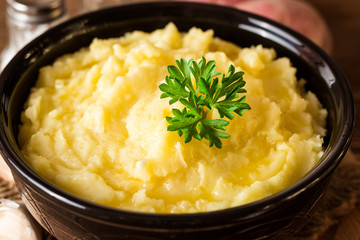 Mashed potatoes with butter and fresh parsley in bowl on rustic wooden table