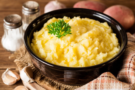 Mashed potatoes with butter and fresh parsley in bowl on rustic wooden table