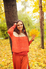 Pretty smiling woman portrait, walking in autumn park, dressed in casual orange sweater and skirt