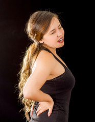Young beautiful sportwoman suffer cervical pain in her lower back, in black background
