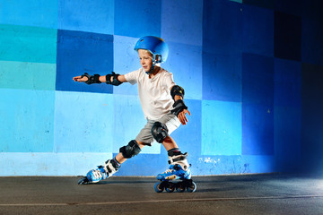 Young boy on roller skates making slide against the blue graffiti wall