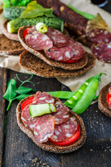 rye sandwich with sausage and tomatoes on wood table