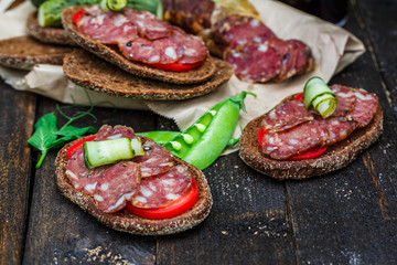 rye sandwich with sausage and tomatoes on wood table