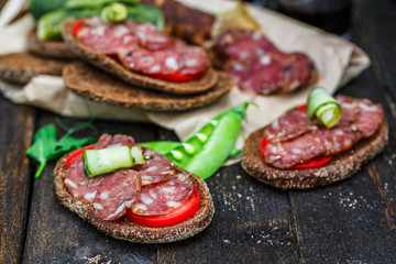 rye sandwich with sausage and tomatoes on wood table